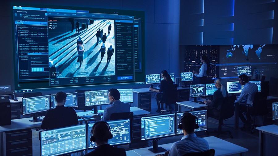 Team of Professional Cyber Security Data Science Engineers Work Team of Professional Cyber Security Data Science Engineers Work on Surveillance Tracking Shot of People Walking on City Streets. Big Dark Control and Monitoring Room with Computer Displays.